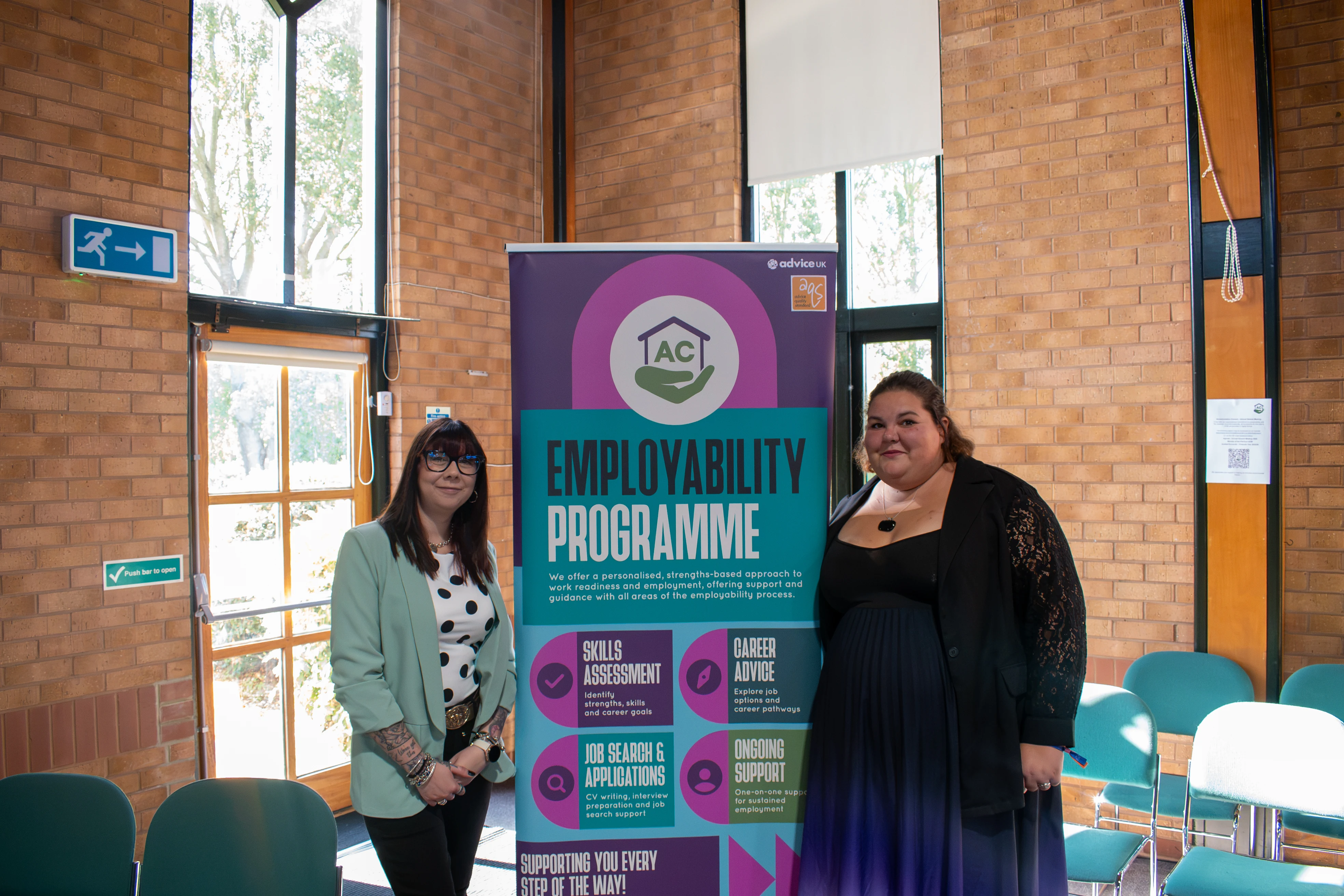 Two attendees beside AC’s employability programme banner at the AGM